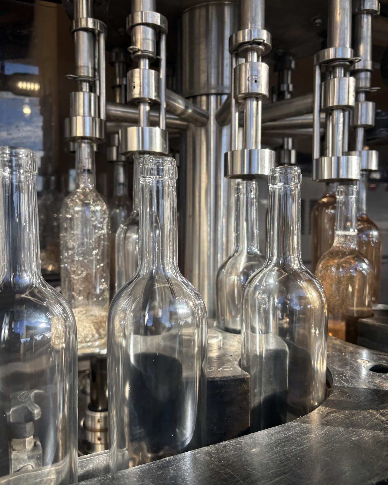 Gros plan sur des bouteilles vides debout sous les becs de remplissage inox.