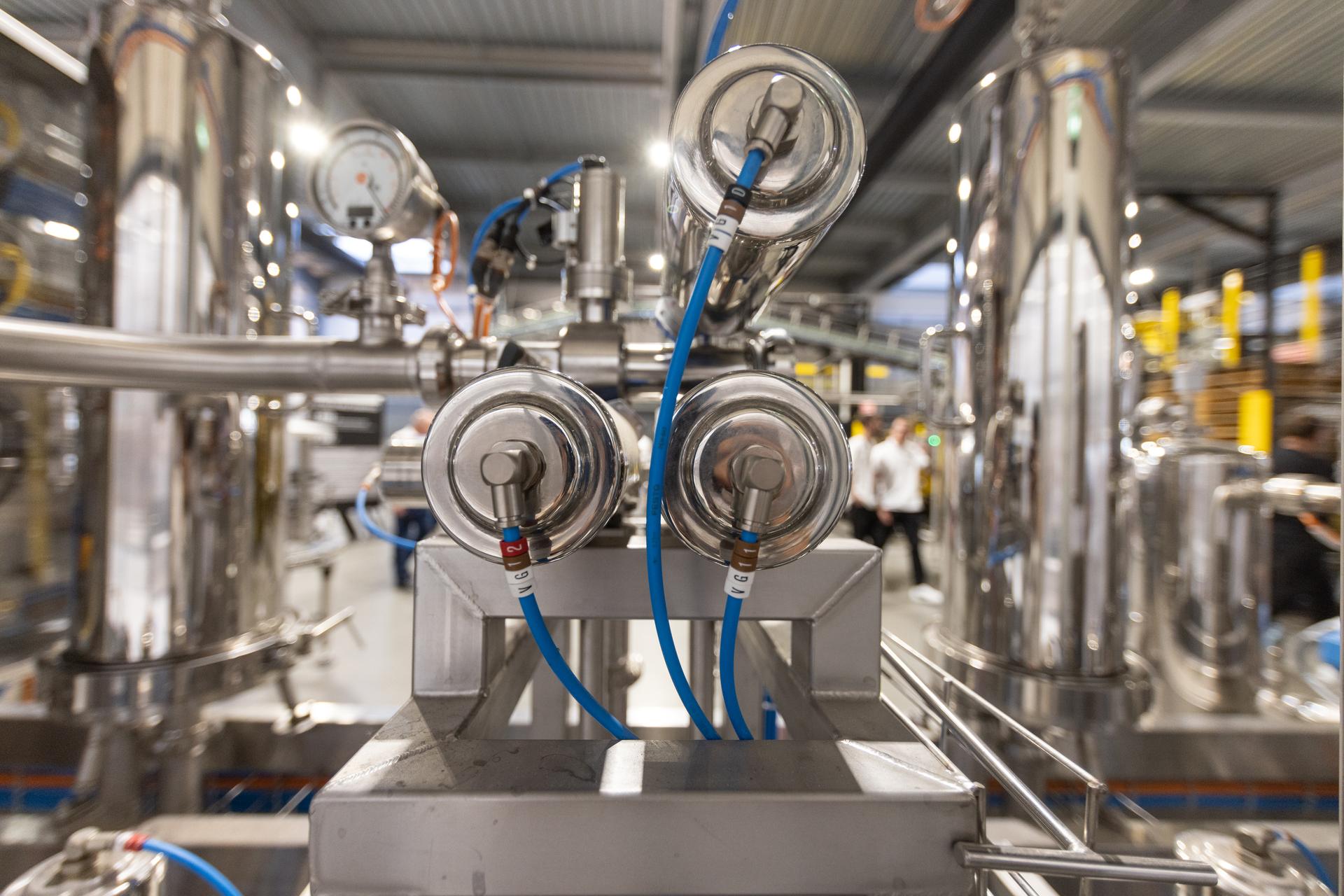 Gros plan sur deux manomètres et des flexibles bleus montés sur un skid inox.